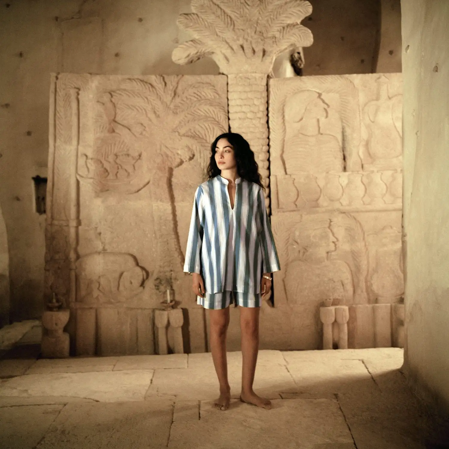 a woman in a blue and white striped dress standing in front of an egyptian statue