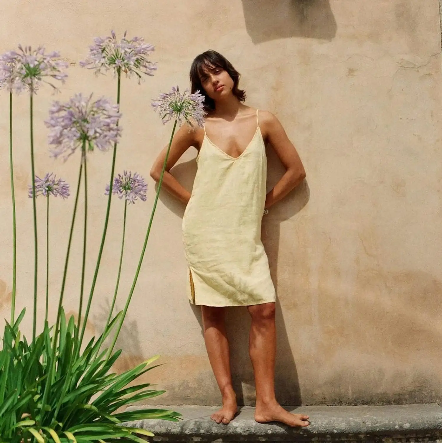 a woman in a yellow dress leaning against a wall